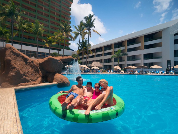 Hombre y mujer con dos niños flotando en sandía inflable en la piscina del resort