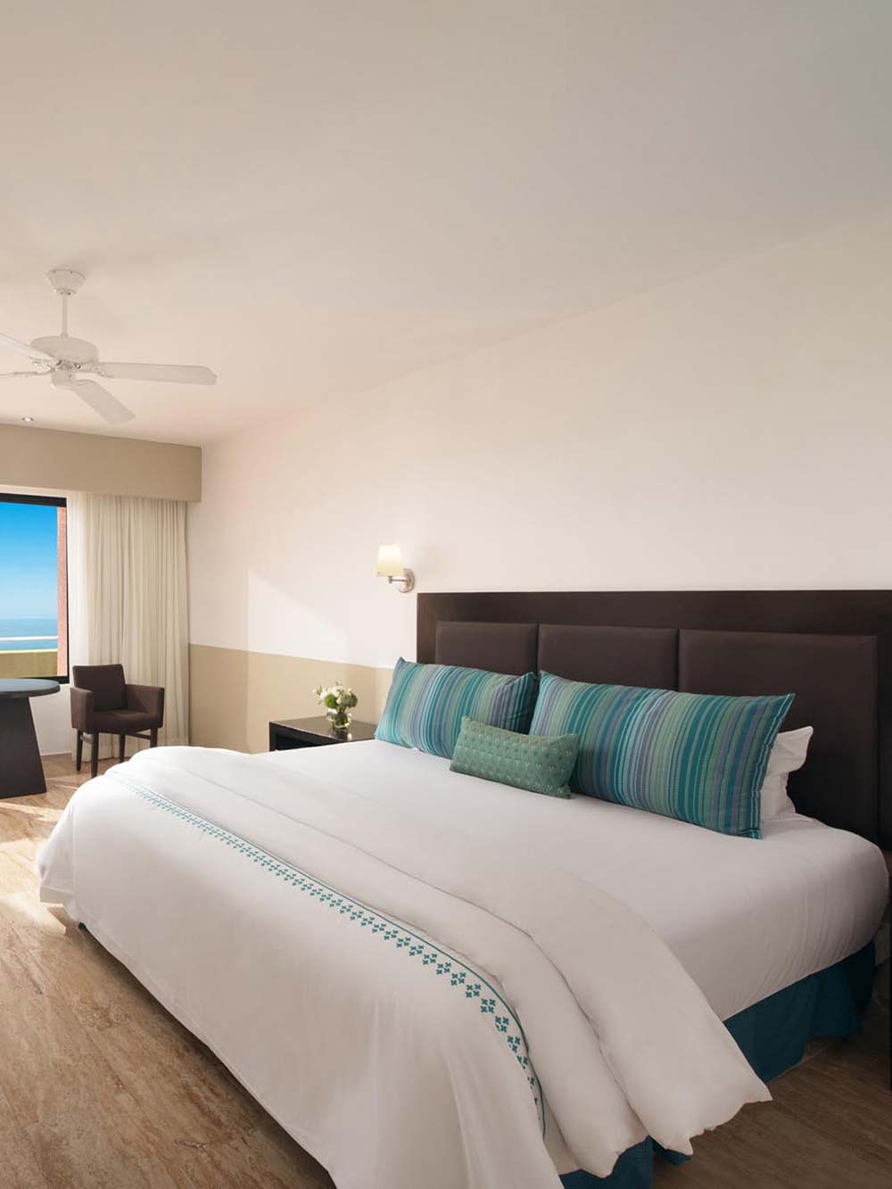 King bed with white sheets, blue pillows, and view of ocean from window